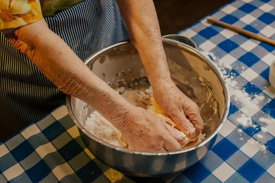 Manos de la abuela amasando en un bol sobre mantel a cuadros